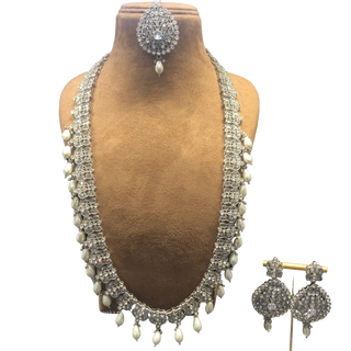 A set of antique silver jewelry including a necklace, earrings, and a tikka, displayed on a mannequin. The jewelry features white pearl-like beads and intricate silver detailing.