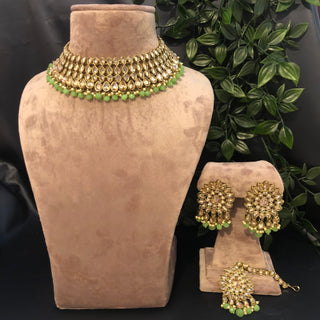 A set of antique gold jewelry including a necklace, earrings, and a tikka, displayed on a mannequin with a green and gold color scheme.